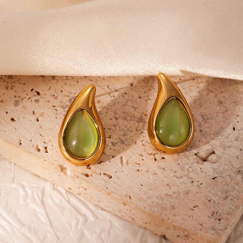 Gold earrings with green stones on a textured beige surface