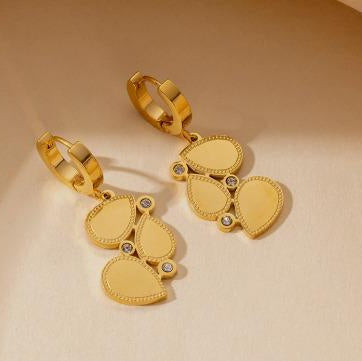 Gold earrings with heart-shaped pendants on a beige background