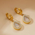 Gold hoop earrings with teardrop-shaped pendants on a beige background