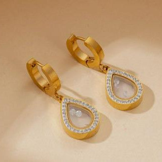 Gold hoop earrings with teardrop-shaped pendants on a beige background