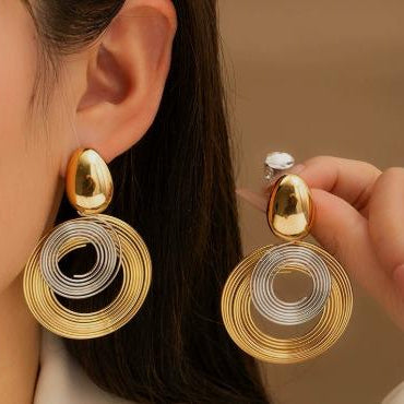 Gold and silver earrings being worn and held by a person against a neutral background