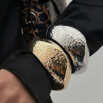 Close-up of a person wearing a black outfit with gold and silver metallic cuffs.