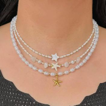 Three pearl necklaces with star-shaped pendants on a person wearing a black top.