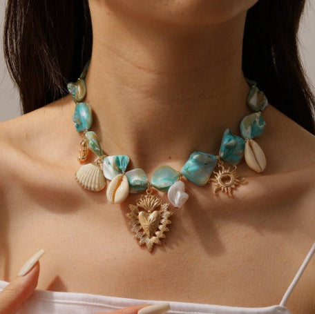 Necklace with turquoise stones, seashells, and gold accents worn by a person.