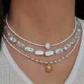Pearl necklaces with a gold pendant on a person wearing a white top.