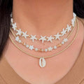 Necklace with starfish and shell designs on a person wearing a brown top.