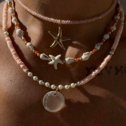 Necklace with starfish and coin pendants on a person's neck