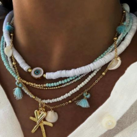 Necklace with multiple strands of beads and charms on a person wearing a white shirt.