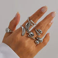 Hand wearing multiple silver rings on a neutral background