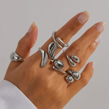 Hand wearing multiple silver rings on a neutral background