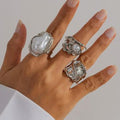 Hand wearing multiple silver rings with pearls on a neutral background