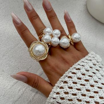 Hand wearing multiple pearl rings on a neutral background