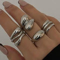Hand wearing multiple silver rings on a neutral background