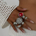 Hand wearing multiple silver rings with a red gemstone on a white background