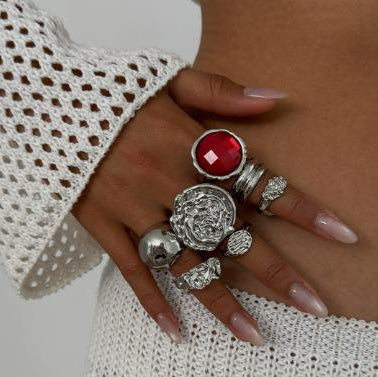 Hand wearing multiple silver rings with a red gemstone on a white background