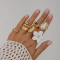 Hand wearing multiple gold rings with a white lace sleeve on a neutral background