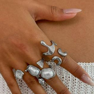 Silver ring with multiple designs on a finger against a neutral background