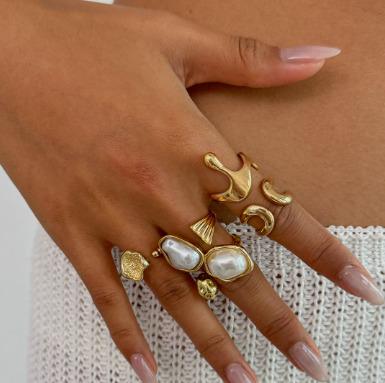 Hand wearing multiple gold rings with pearl accents on a neutral background
