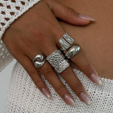 Hand wearing multiple silver rings on a textured white fabric background