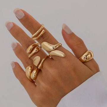 Hand wearing multiple gold rings on a plain background