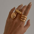 Hand wearing three gold rings on a neutral background