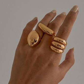 Hand wearing three gold rings on a neutral background