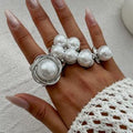 Hand wearing multiple pearl rings on a light background