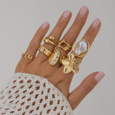 Hand wearing multiple gold rings with a plain background