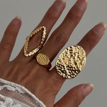 Hand wearing two gold rings on a neutral background