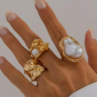 Hand wearing two gold rings with pearl-like stones on a neutral background