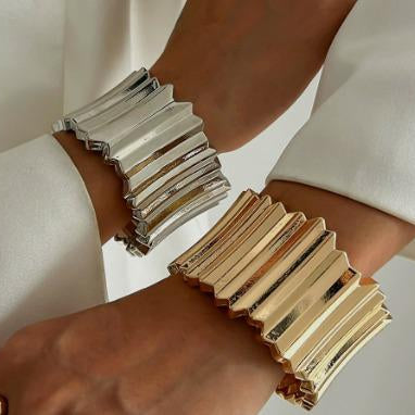 Two wrists wearing gold and silver bracelets on a white background