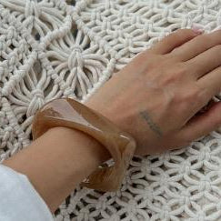 Hand wearing a clear bracelet on a textured white surface
