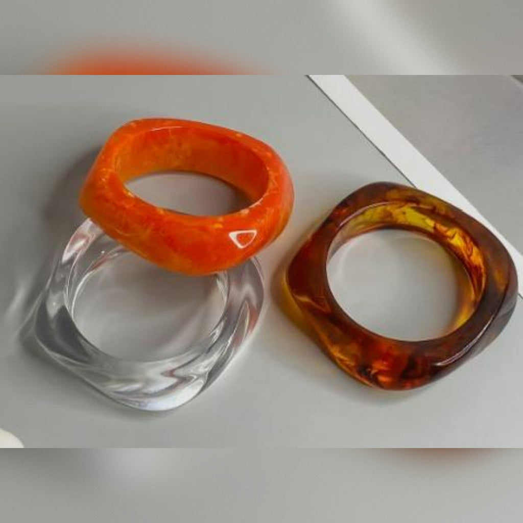 Three glass rings in orange, clear, and brown on a light gray background